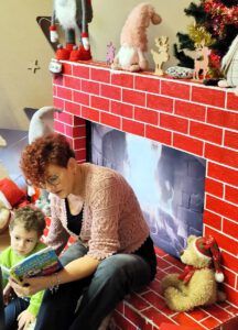 Pani czytająca dziecku książkę przy kominku.