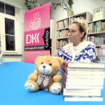 Miś ustawiony przy książkach w tle kobieta w okularach i rolap z DKK.