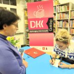 Kobieta stojąca przed autorką składającą autograf w książce.