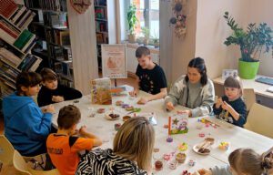 Na zdjęciu widać osoby siedzące przy stole pełnym pojemniczków z koralikami.