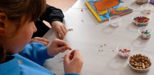 Fotografia przedstawia zdjęcie rączek nawlekających koraliki.