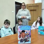 Na fotografii widoczna okładka książki, dzieci i Pani Dyrektor