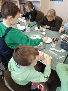 Grupa dzieci tworzy pracę . W tle widać regały z książkami.