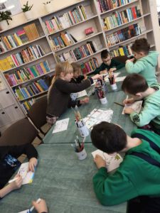 Grupa dzieci tworzy pracę . W tle widać regały z książkami.