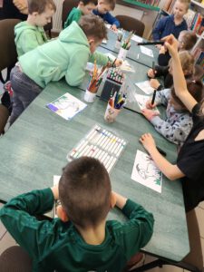 Grupa dzieci tworzy pracę . W tle widać regały z książkami.