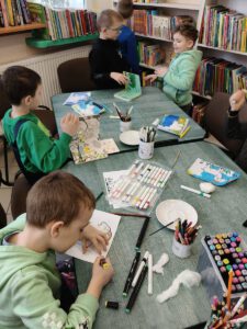 Grupa dzieci tworzy pracę . W tle widać regały z książkami.