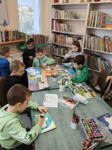 Grupa dzieci tworzy pracę . W tle widać regały z książkami.