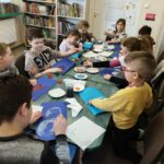 Dzieci malują farbami po niebieskich kartkach.