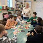 pani w białej bluzie opowiada o zdrowym odżywianiu , na stole leżą magnesy przypominające żywność.