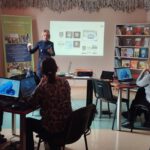 Na zdjęciu widzimy Panią przemawiającą do uczestników warsztatów komputerowych.