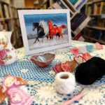 Na stole ułożone prace pani Ani, w oddali widać obraz trzech biegnących koni.