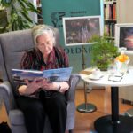 Starsza pani siedząca w fotelu, czytająca dzieciom bajkę.