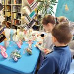Dzieci stojące przy stole, oglądające prace rękodzielnicze.