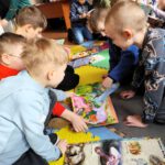 Dzieci siedzące na matach oglądające książki.