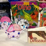 Fotografia przedstawia książki o dinozaurach i wykonane prace.