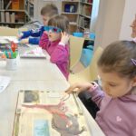 Na zdjęciu widoczna trójka dzieci oglądających książki o dinozaurach.