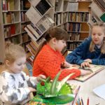 Fotka przedstawia dziewczynkę, która przegląda książkę z odstającymi elementami dinozaurów.