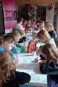 Na zdjęciu widoczna grupa dzieci siedzących przy stole, kolorujących prace wielkanocne.