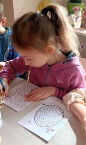 Zdjęcie przedstawia dziewczynkę kolorującą kredkami.