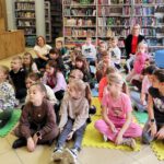 Grupa dzieci siedząca na piankach, wśród nich siedzą dwie kobiety.