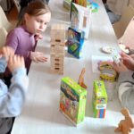 Fotografia przedstawia dzieci siedzące przy stole i grające w gry.