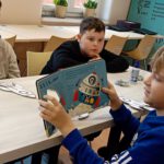 Na zdjęciu chłopczyk czyta książkę na której widać obrazek rakiety.