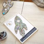 Na zdjęciu widoczna ramka z ologowaniem i wykonaną rakietą oraz rączki dzieci wyklejające rakiety.