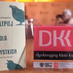 Książka ze stojakiem na którym widniej napis Dyskusyjny Klub Książki w tle widać uczestniczki